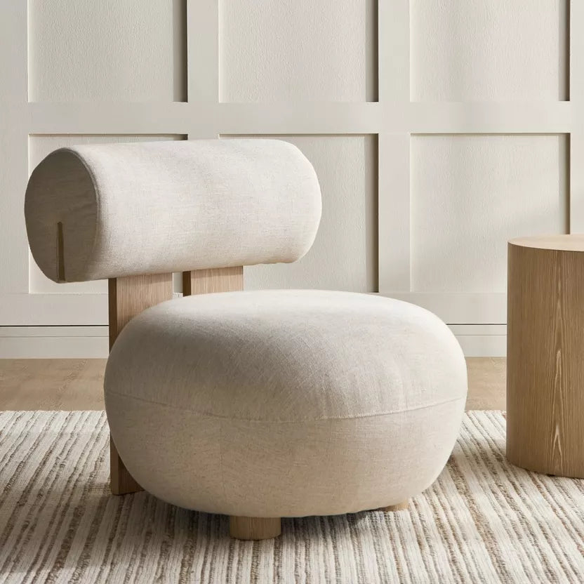 Modern beige chair with wooden legs in a room with paneled walls and a wooden side table.